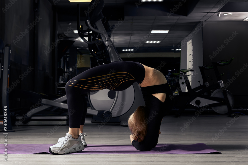 Sporty girl does stretching exercises in gym stands on the bridge, stretches her back Sporty girl does stretching exercises in gym stands on the bridge, stretches her back