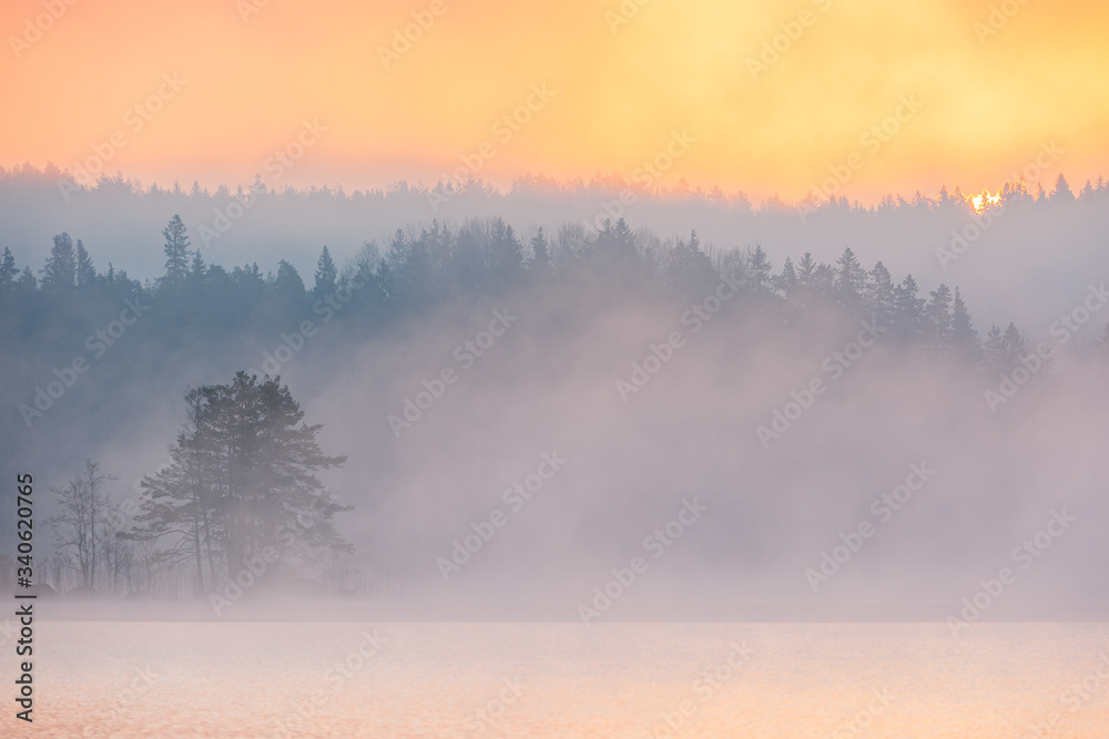 Sun rising above forest and misty lake, Sweden.