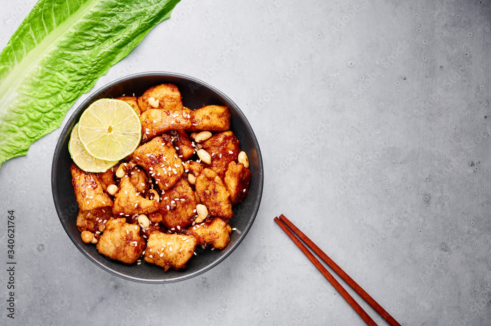 Fototapeta premium Korean Sweet Fried Chicken Dakgangjeong in black bowl at grey concrete background. Dakgangjeong is korean cuisine dish with deep fried crunchy chicken in sweet sauce. Korean Food