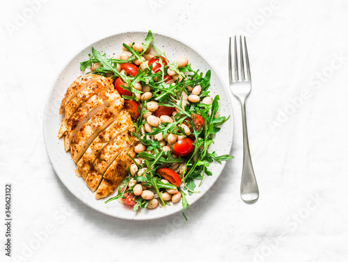 Healthy lunch - roasted chicken breast and white beans, arugula, cherry tomatoes salad on a light background, top view