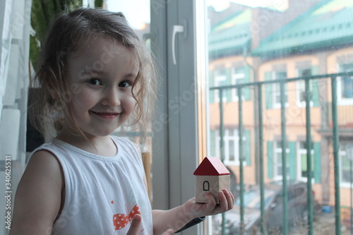 The girl is holding a wooden house on her palm. Looks out the window at the street. Stay at home during the pandemic. The concept of self-isolation at home, as a way to combat an outbreak of coronavir photo