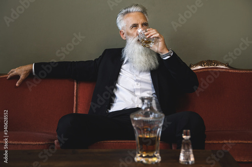Fotografi Handsome bearded senior man drinking whiskey