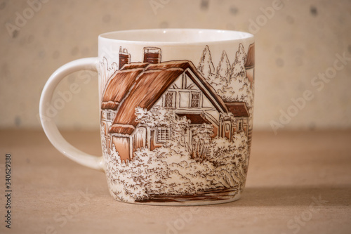 A large ceramic mug with a beautiful pattern, a house and trees, as if a village house.