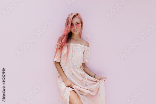 Winsome young woman in sunglasses playing with her romantic dress. Portrait of fascinating girl with pink hair isolated on white background.