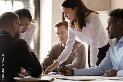 Multicultural businesspeople gather at office table brainstorm discuss paperwork together at briefing, focused diverse multiracial colleagues consider statistics at meeting, collaboration concept