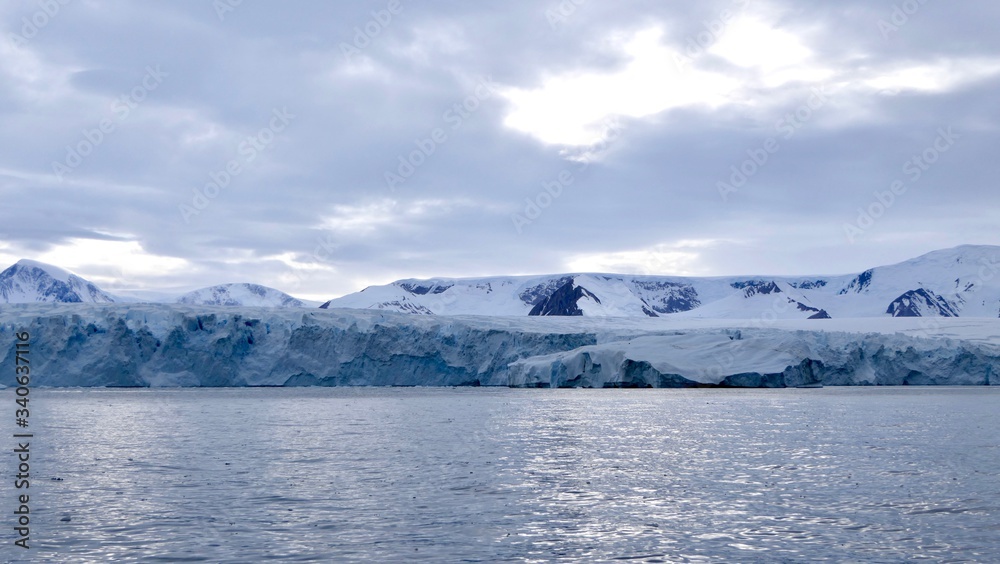 Glacier front in antarctic sea with cloudy sky, ocean with light reflections, Antarctica