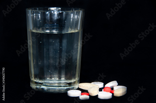 glass of water and pills. pills on a black background.