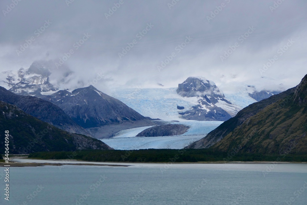 Glacier in chilean fjord with blue ice, high mountain and clouds, glacier alley, Beagle Channel