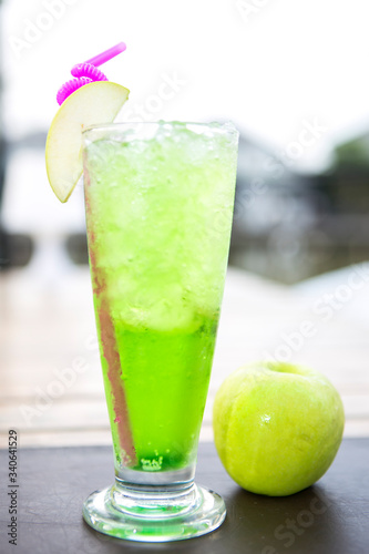green apple juice drink in a tall glass decorated with sliced green apple next to a green apple depth of field background