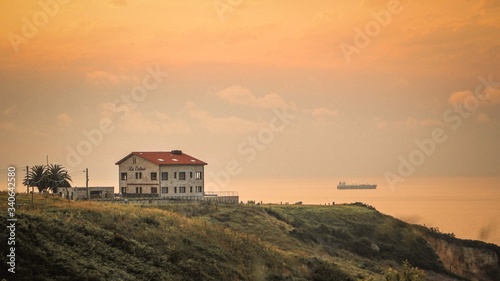 Casa al borde del acantilado en un atardecer y un barco al fondo