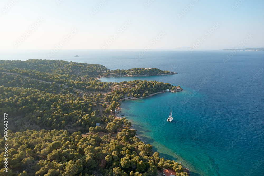 White catamaran in turquoise tropical water with green forest behind. Catamaran sailing on turquoise waters