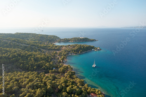 White catamaran in turquoise tropical water with green forest behind. Catamaran sailing on turquoise waters