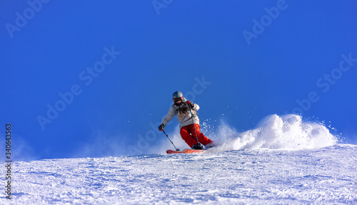 Girl On the Ski. a skier in a bright suit and outfit with long pigtails on her head rides on the track with swirls of fresh snow. Active winter holidays, skiing downhill in sunny day. Woman skier photo