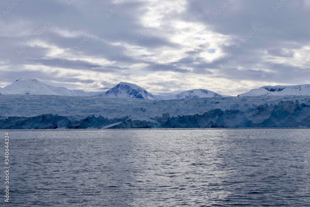 Glacier front in antarctic sea with light reflections on dark ocean and cloudy sky, Antarctica