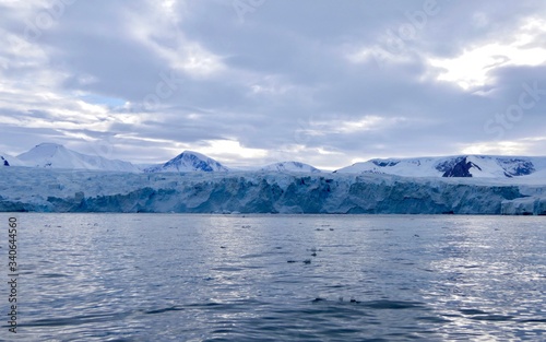 Glacier front in antarctic sea with cloudy sky and ocean with light reflections, Antarctica