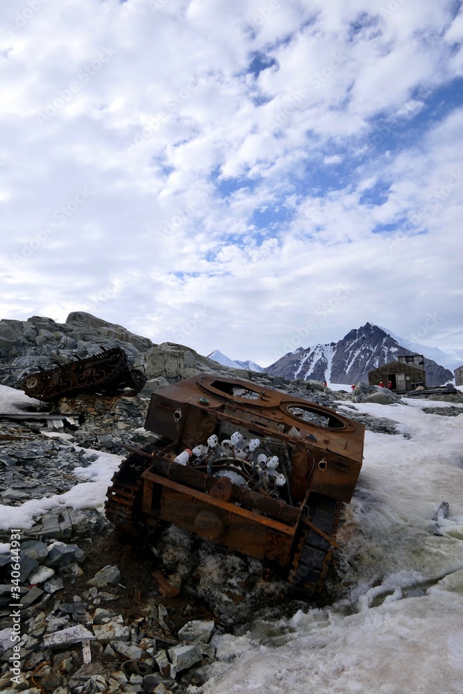 Rusty tank wreck in Antarctica, at Stonington Island, with east base, mountain and explorers in background Rusty tank wreck in Antarctica, at Stonington Island, with east base, mountain and explorers in background