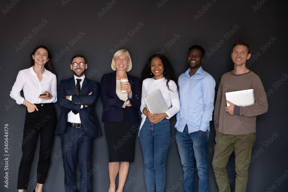 Group picture of smiling multiethnic diverse businesspeople stand posing near black wall look at camera together, happy multicultural employees make team photo at workplace, unity, teamwork concept