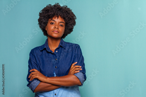 Black young woman with glasses with black power hair wearing blue jeans shirt on blue background, serious