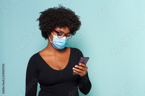 black woman with black power hair wearing protective mask with smartphone in hands and wearing reading glasses photo