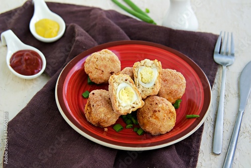 Scottish eggs, boiled quail eggs in minced chicken on a red clay plate on a light concrete background. Can be served as a starter or main course. Recipes with eggs.