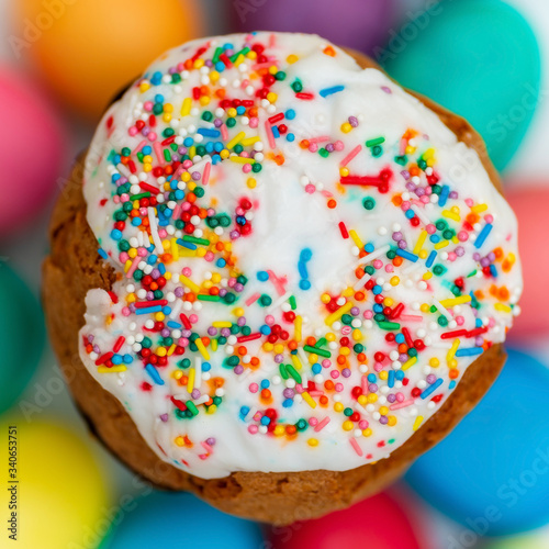 View of an Easter cake with white icing and colored sprinkles  on a blurry background of colored eggs