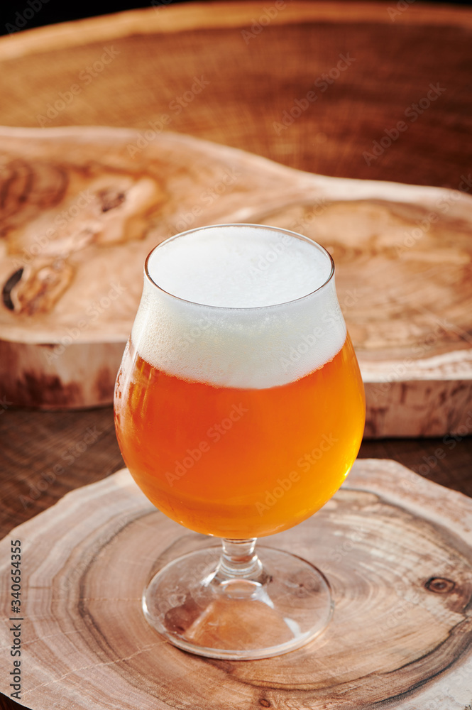 Light beer with foam in a round beer glass (snifter) on a leg on a wooden background. Close up. Light beer with foam in a round beer glass (snifter) on a leg on a wooden background. Close up.