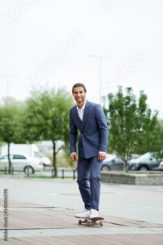 Attractive bearded young man in classic suit on skateboard. Eleg