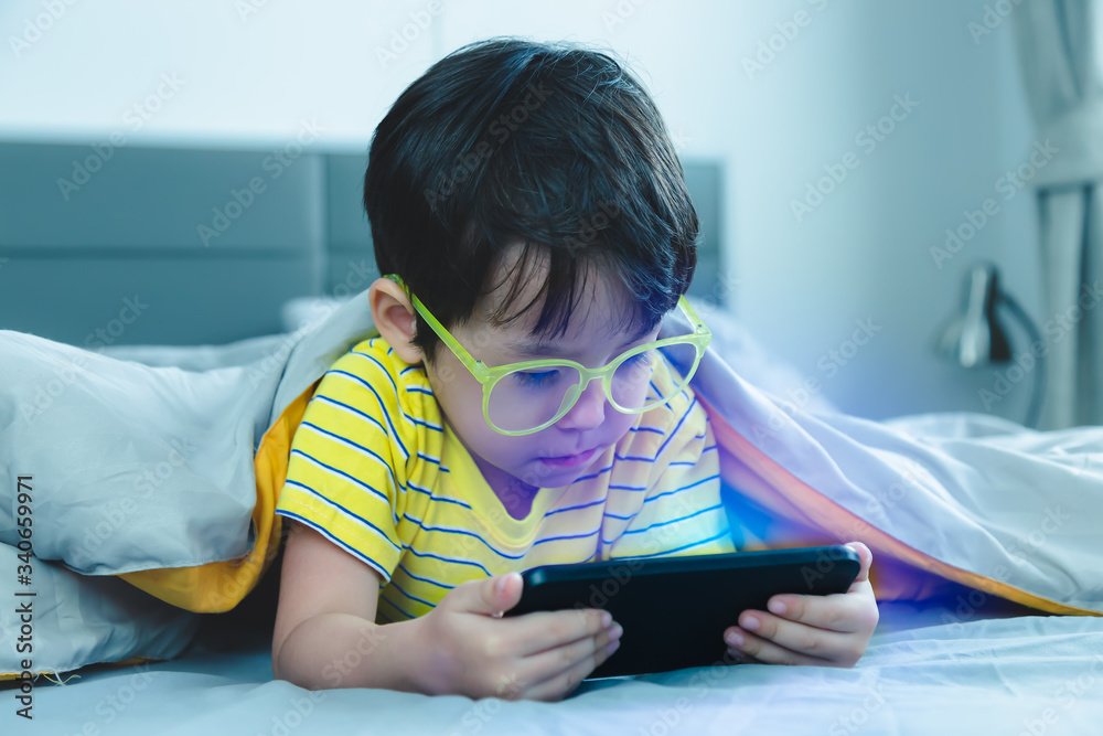 Cute little child watch movie on smartphone on bed. Dangers of blue light  is damaged eyes.