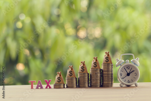 Finance tax concept: Words tax, alarm clock, US money bags on rows of rising coins. depicts ad valorem tax on value of a property