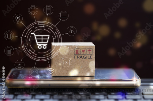 Online shopping, e-commerce concept: Cardboard box with smartphone on notebook keyboard and icon customer network connection. Product service and delivery to consumers by connecting with the internet. photo