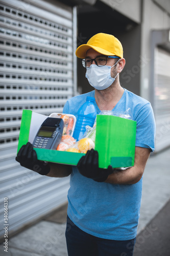 Delivery guy with protective mask holding box / bag with groceries and POS for contactless payment.