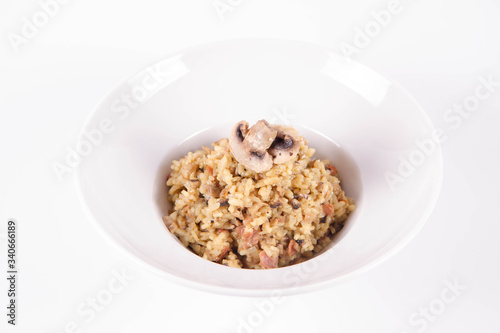 Risotto with button mushroom and bacon decorated with mushroom on a plate on a white background