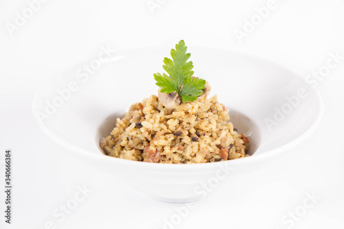 Risotto with button mushroom and bacon decorated with parsley on a plate on a white background
