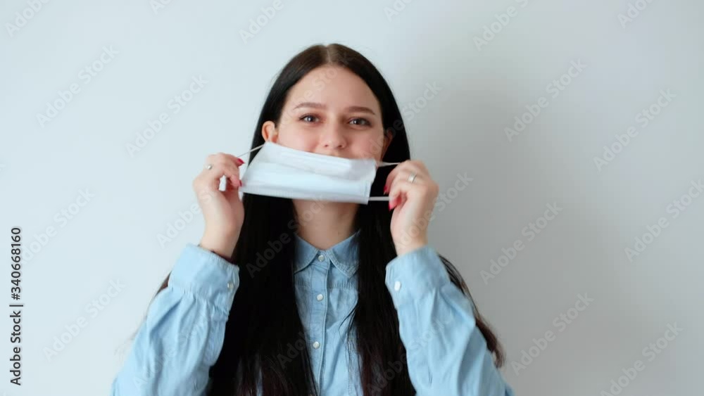 closeup of a young smiling woman girl putting on a medical protective mask, looking at the camera, hygiene concept covid-19, coronavirus, on a white background, unsuccessful take, laugh closeup of a young smiling woman girl putting on a medical protective mask, looking at the camera, hygiene concept covid-19, coronavirus, on a white background, unsuccessful take, laugh