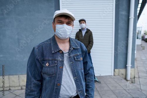 man and teen boy posing near wall and closed door of high-rise buildings with apartments, a residential area, a medical mask on their faces protects against viruses and dust