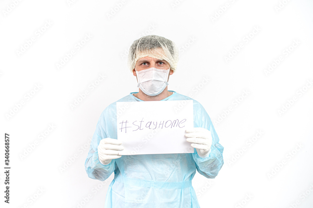 The doctor on a blue background in a medical gown in a surgical mask and cap calls Stay home. COVID-19. Self isolation. Stay home, conception. Quarantine.