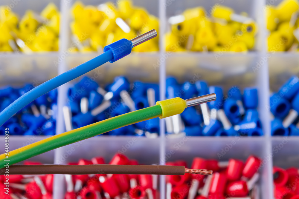 Colorful insulated crimp ends of power cables or brown stripped copper wire. Crimped connector electric joins. Ferrule pin cord terminals organized in plastic grid of tool box detail. Selective focus.