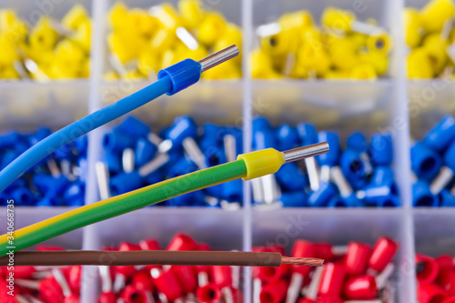 Colorful insulated crimp ends of power cables or brown stripped copper wire. Crimped connector electric joins. Ferrule pin cord terminals organized in plastic grid of tool box detail. Selective focus.