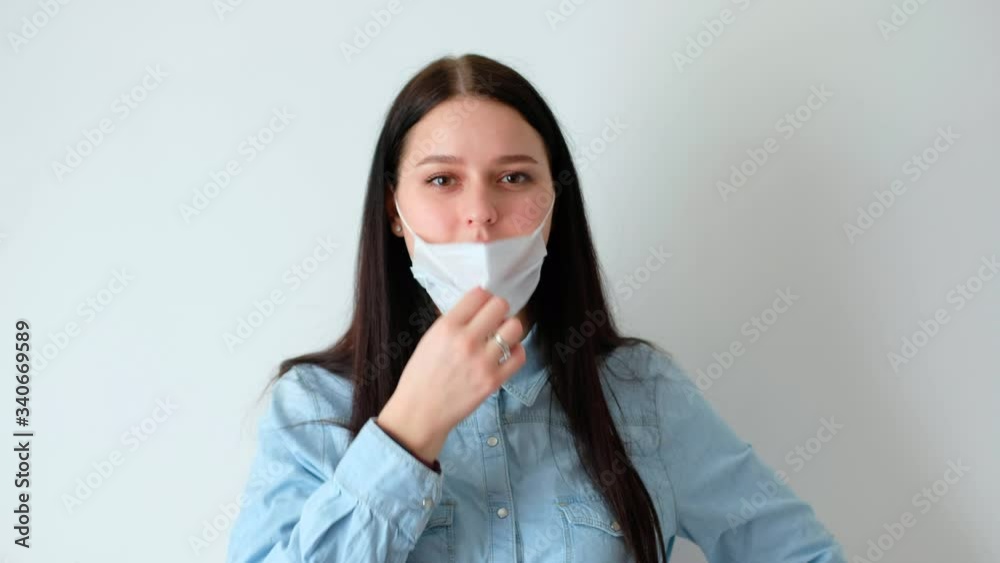 closeup of a young smiling woman, a girl with long brown hair takes off a medical protective mask, sighs heavily, looks at the camera, concept of hygiene covid-19, coronavirus, on a white background