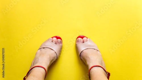 Female legs and summer open toes shoes on colorful background. Yellow background, free copy space. Overhead shot of elegant shoes of pastel color. Top view