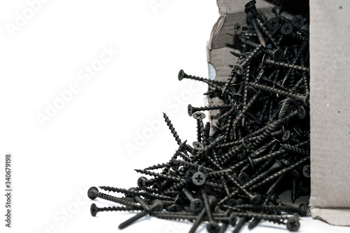 a bunch of new metal black screws poured out of the box on a white background.