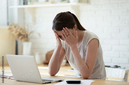 Upset woman touching head using calculator and laptop for calculating finance. Frustration young housewife with headache taxing  accounting  statistics and credit analytic for mortgage payment.