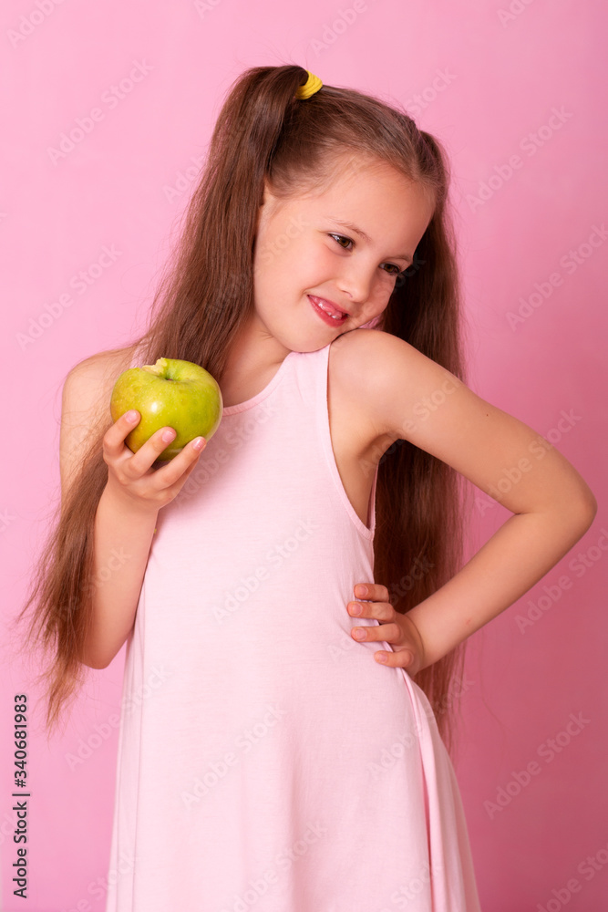 Smiling Girl Holding Apple Looking At Camera Standing On pink Background. Smiling Girl Holding Apple Looking At Camera Standing On pink Background.