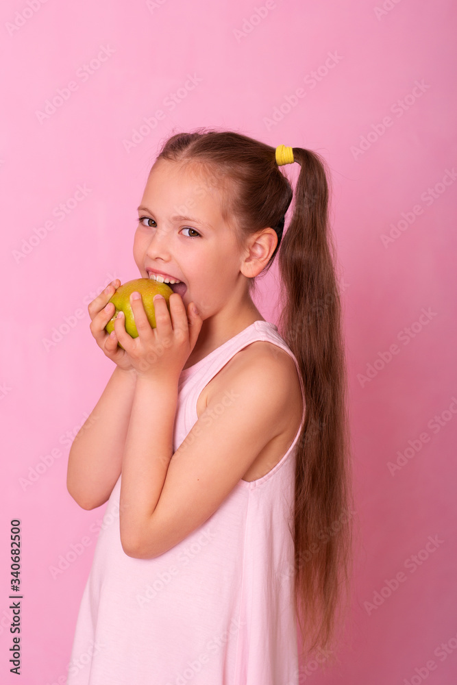 6 year old girl on pink background eats a green apple and smiles. 6 year old girl on pink background eats a green apple and smiles.