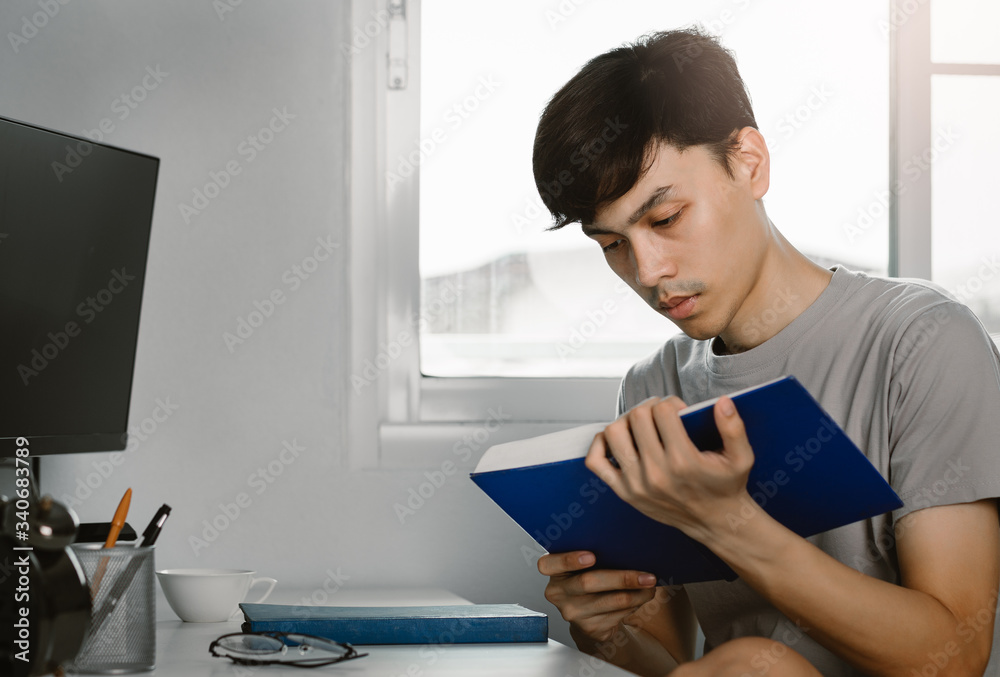Young handsome asian man reading book at work desk in free time from working at home, Knowledge and learning concept.