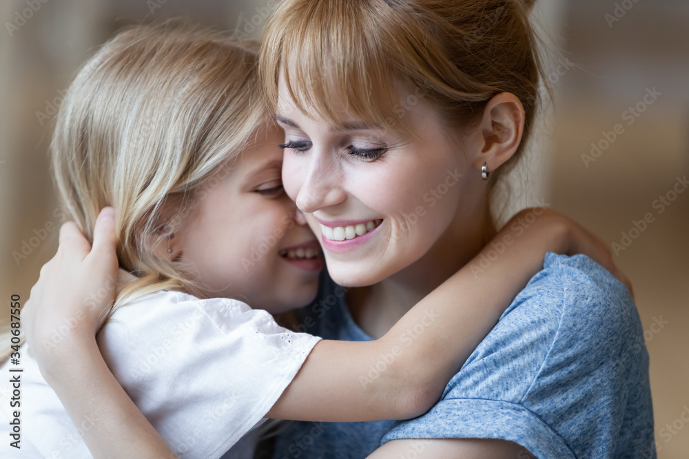 Close up smiling young mother hugging cute preschool daughter. Smiling attractive mom closed eyes embracing little girl enjoying free time together sitting in living room at home.
