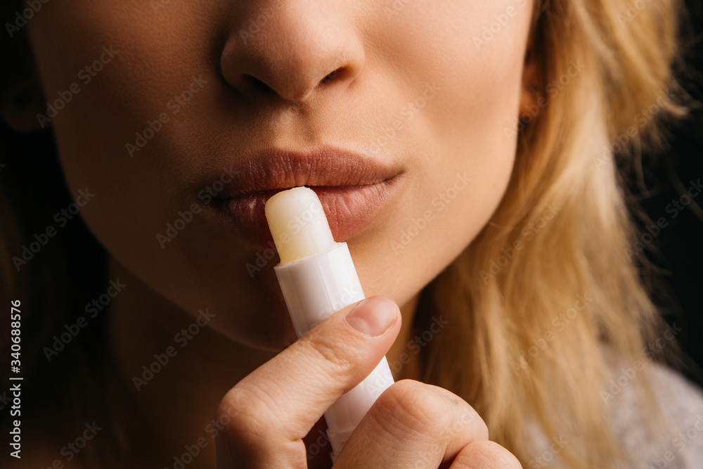 Young woman hold lipstick close to lips. Applying it for hydration. Close up and cut view of cosmetics or make up. Isolated over black background. Young woman hold lipstick close to lips. Applying it for hydration. Close up and cut view of cosmetics or make up. Isolated over black background.