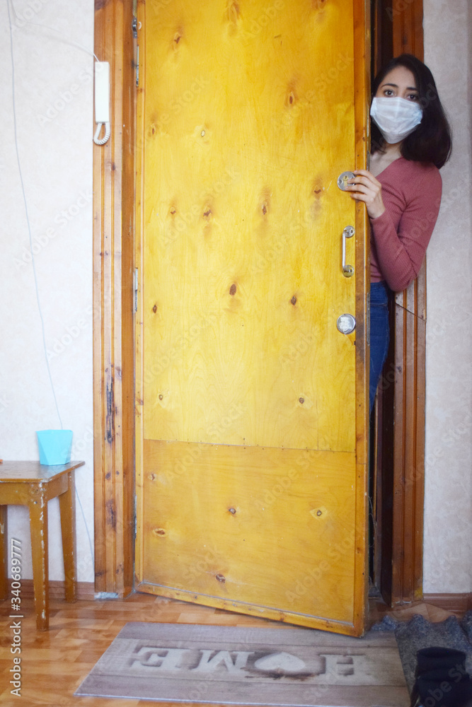 young woman with face mask leaning out door