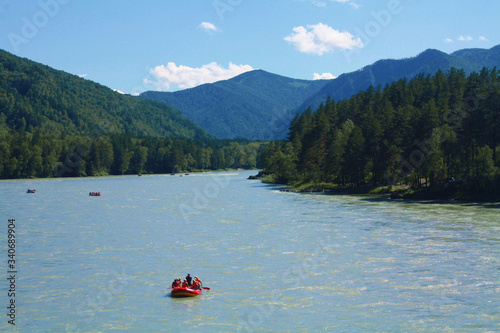 Rafting on the Katun River. A red boat with people rafting along a wide and raging river. Entertainment and tourism in Altai Krai, Russia. Water adventures for extreme sports enthusiasts