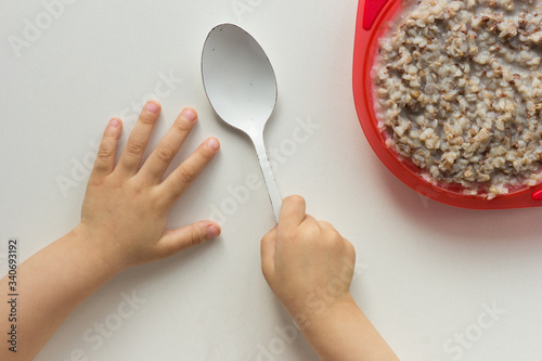 Top view of child hands holding spoon in right hand and buckwheat porridge on the white background photo
